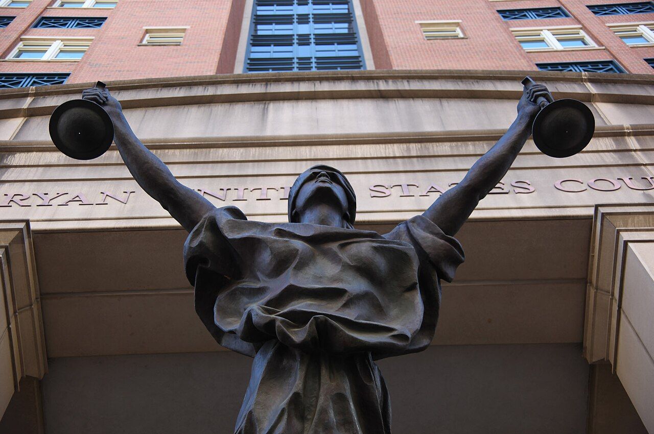 Statue of Justice holding balanced scales and a sword, blindfolded, on a stone building