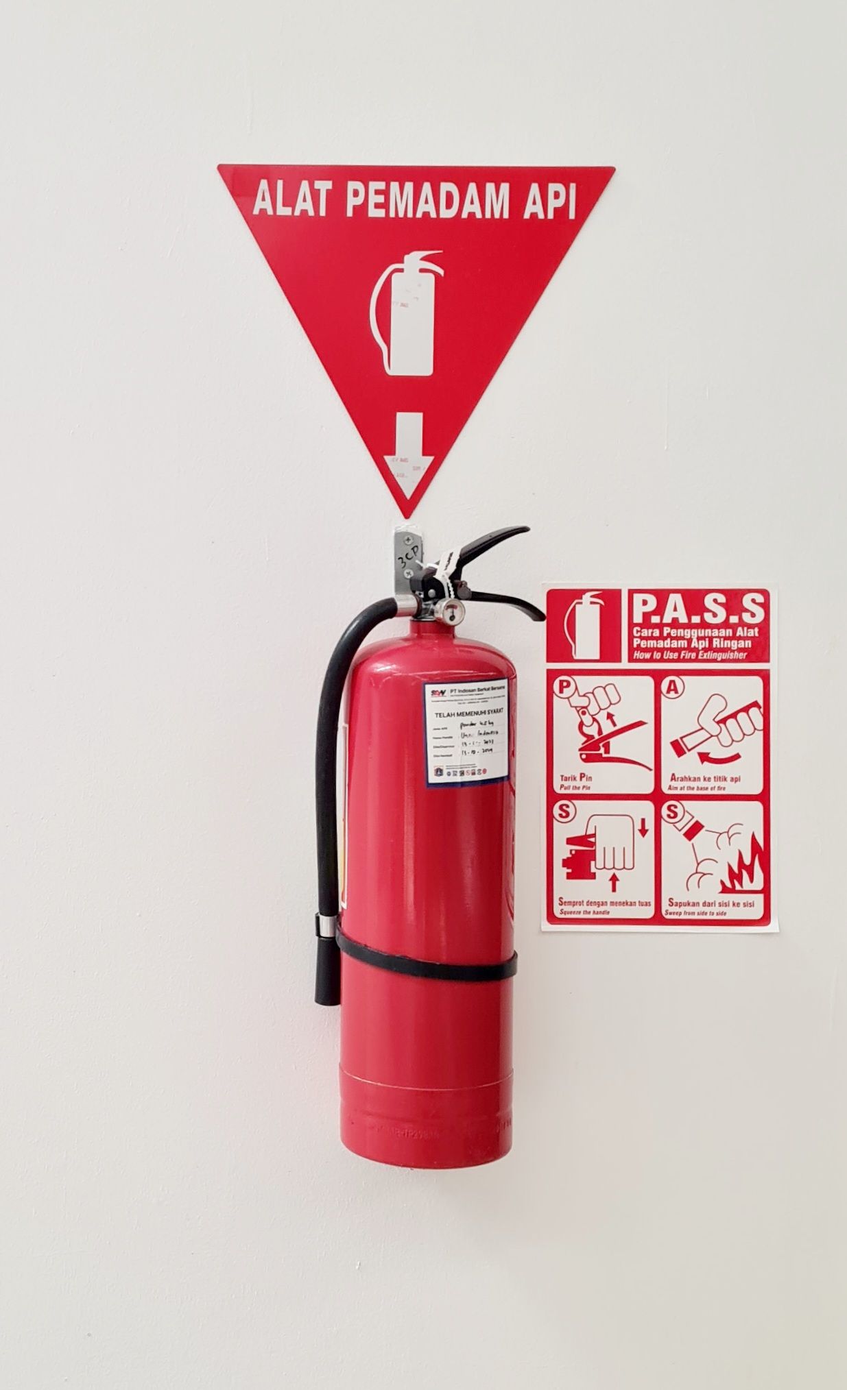 A wall-mounted fire extinguisher instruction plate showing numbered pictorial steps for pulling the pin, aiming, squeezing and sweeping